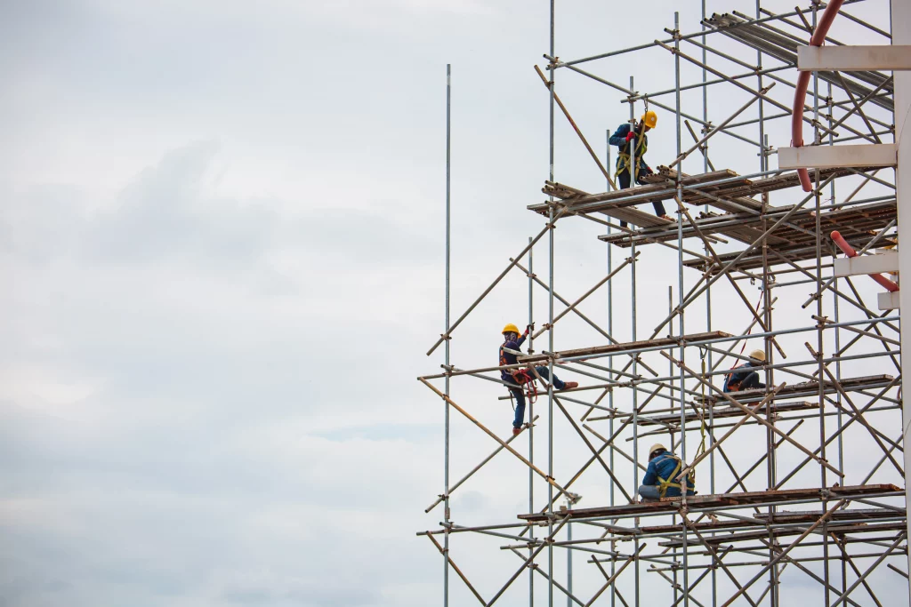 Trabajadores ejecutando el plan de montaje y desmontaje para andamios con medidas de seguridad, arnés y casco en estructura elevada